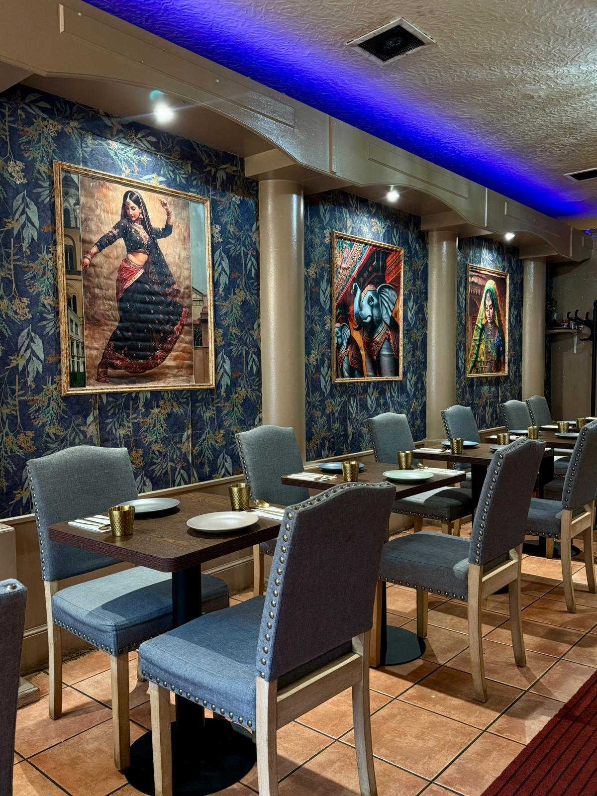 Row of set tables with grey studded chairs, framed paintings of a dancer and elephants along the wall
