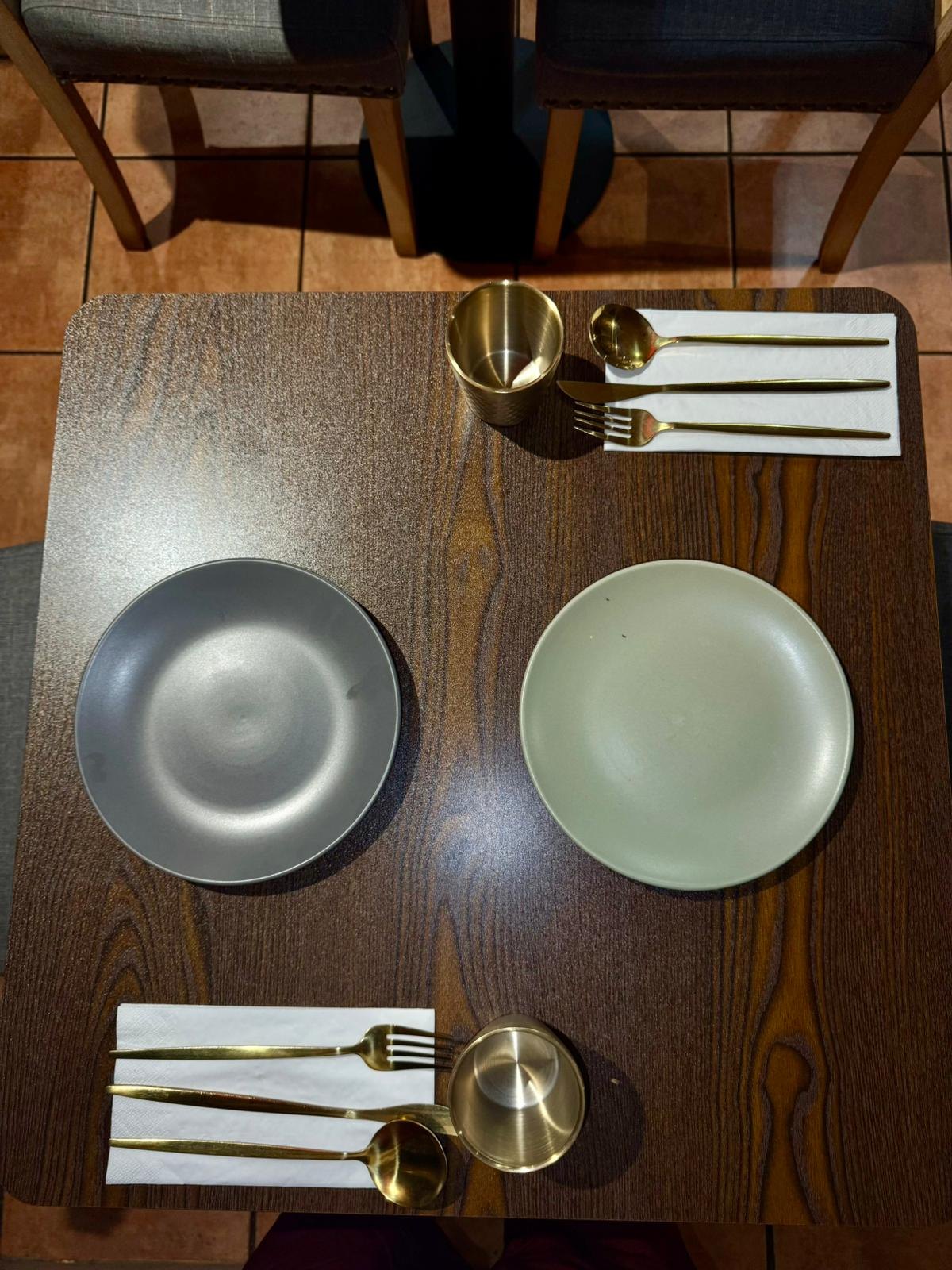 Overhead view of a table for two with grey and sage plates, gold cutlery and tumblers