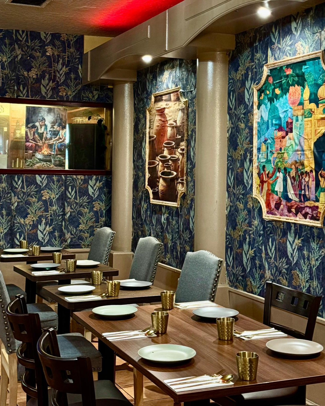 Dining room at Gumnam: tables set with gold tumblers beneath framed Indian artwork on navy botanical wallpaper