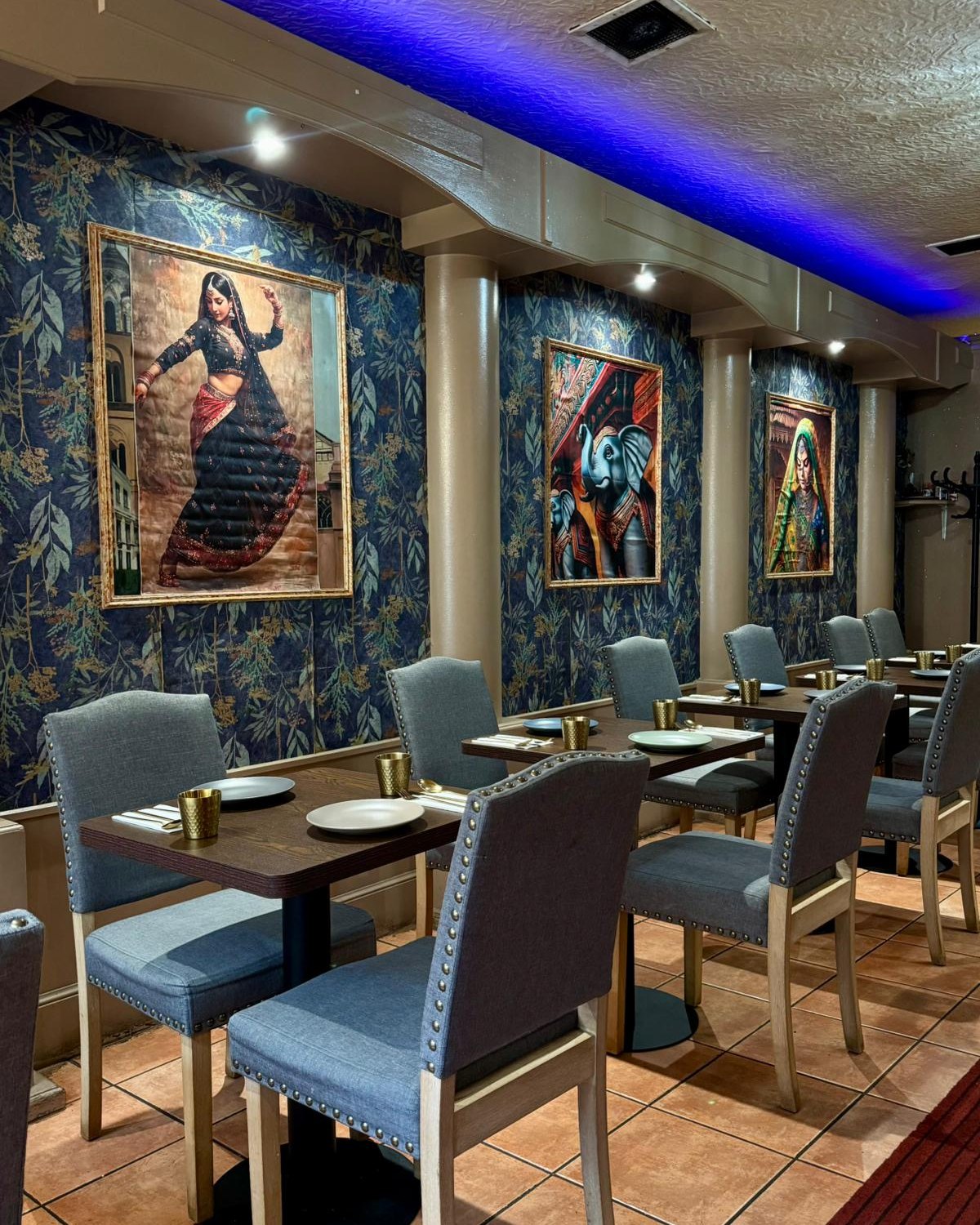 Row of set tables with grey studded chairs, framed paintings of a dancer and elephants along the wall